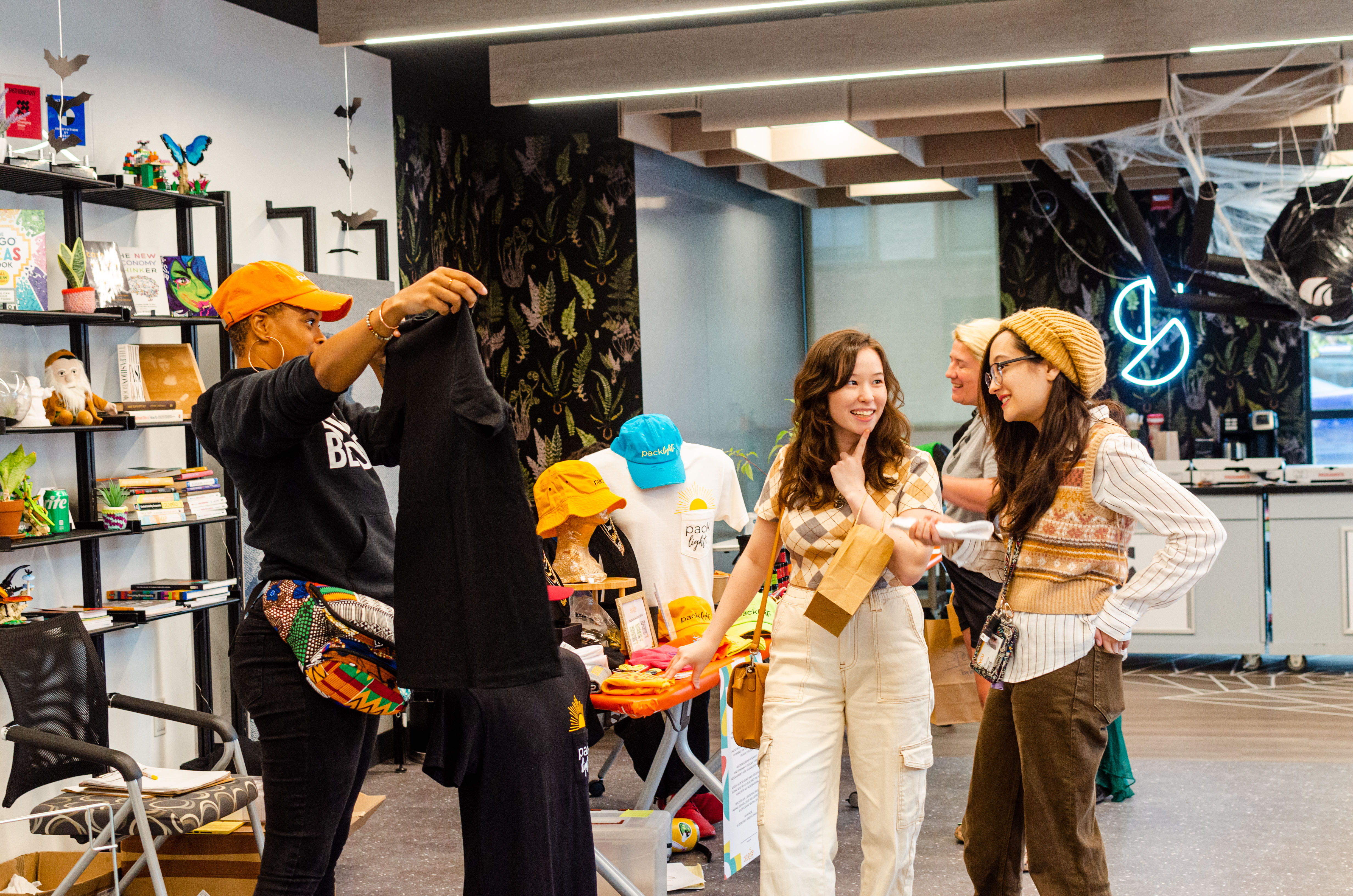 Two young woman look at a black t-shirt and talk to the owner who is holding it up in Shift Retail Lab.